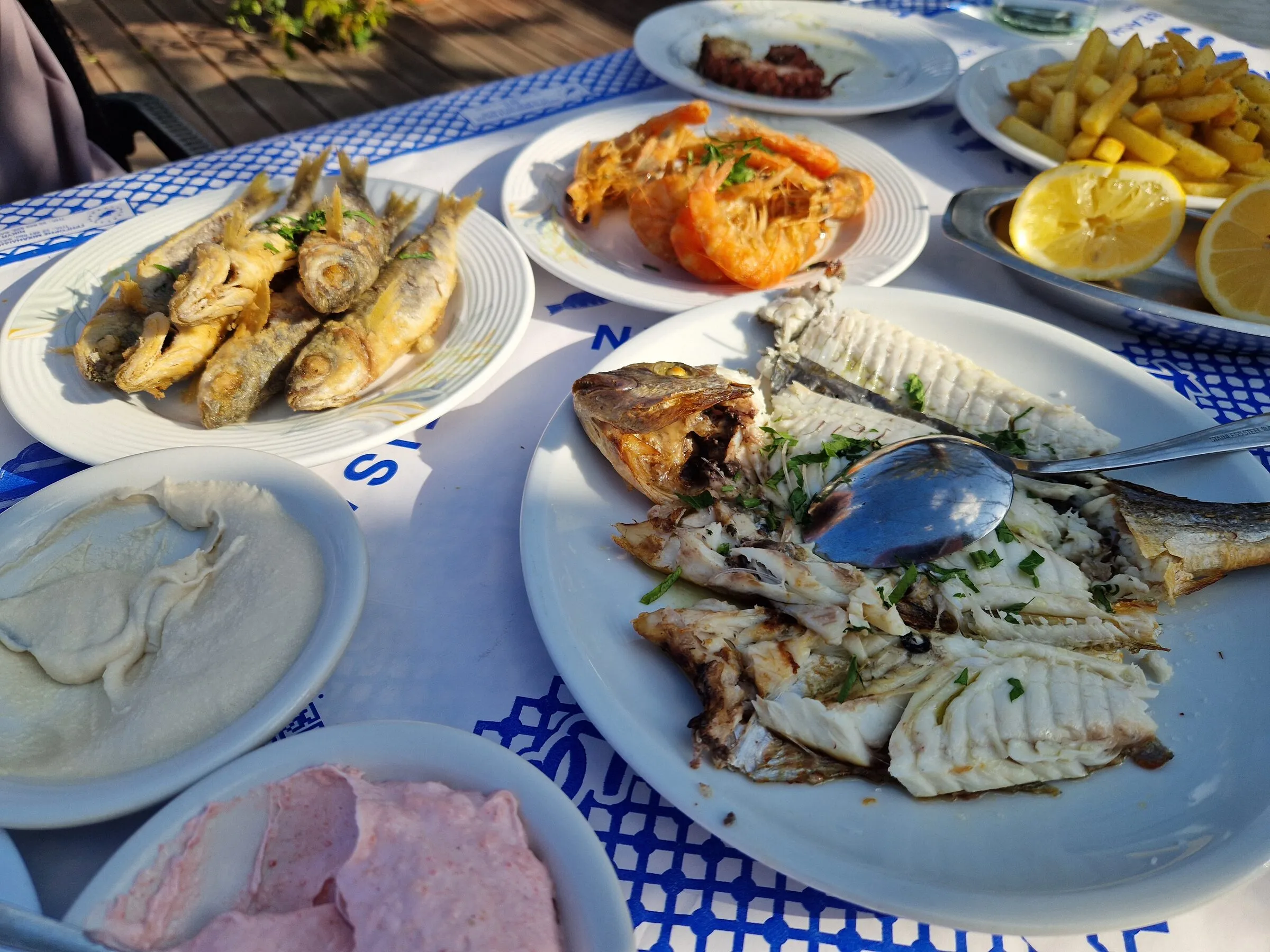 A Mediterranean fish mezze spread of grilled fish, prawns, dips and lemon on a taverna table
