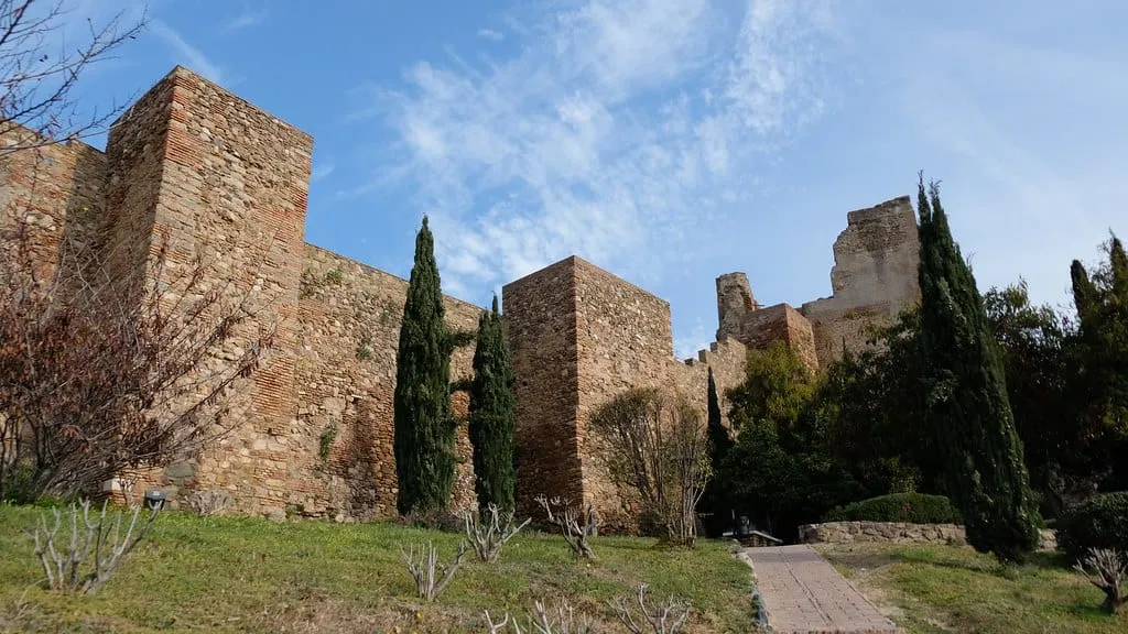 The stone walls and towers of the Alcazaba fortress in Málaga, with cypress trees in front