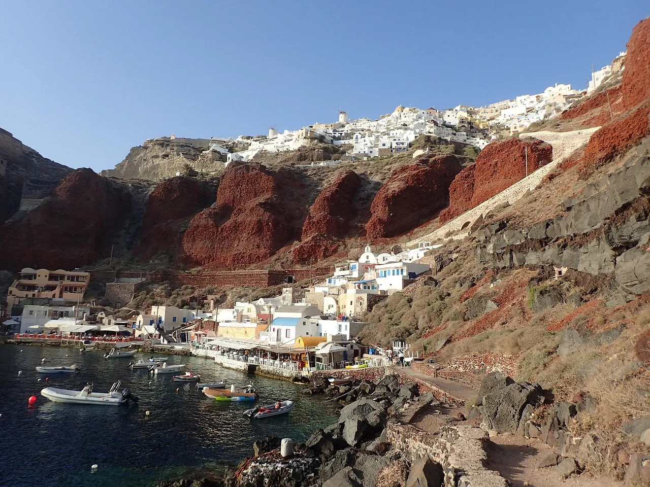 Boats moored on the water below the cliff of the old port of Santorini